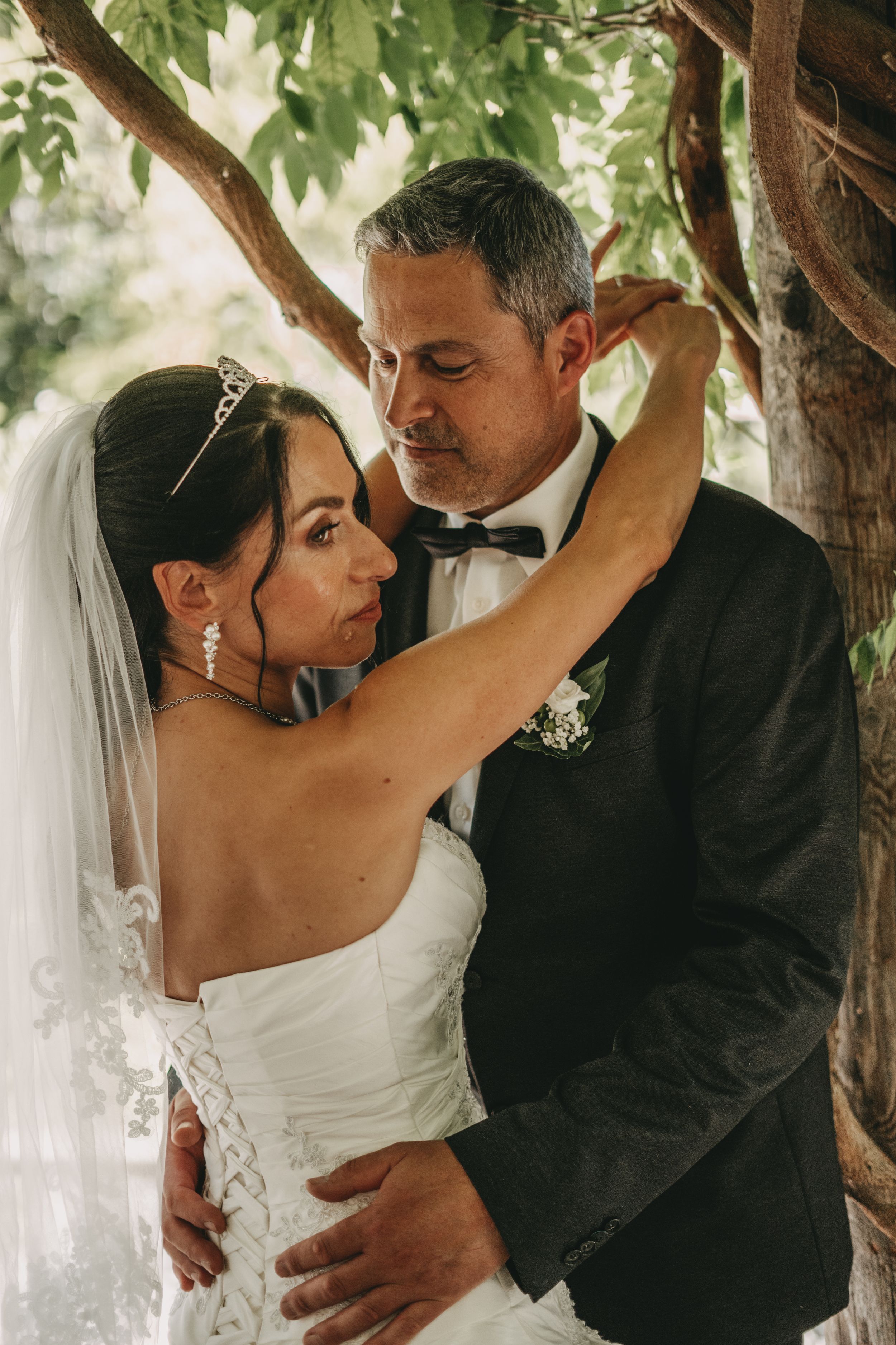 Romantic wedding portraits under tree branches showing tender embraces between newlyweds.