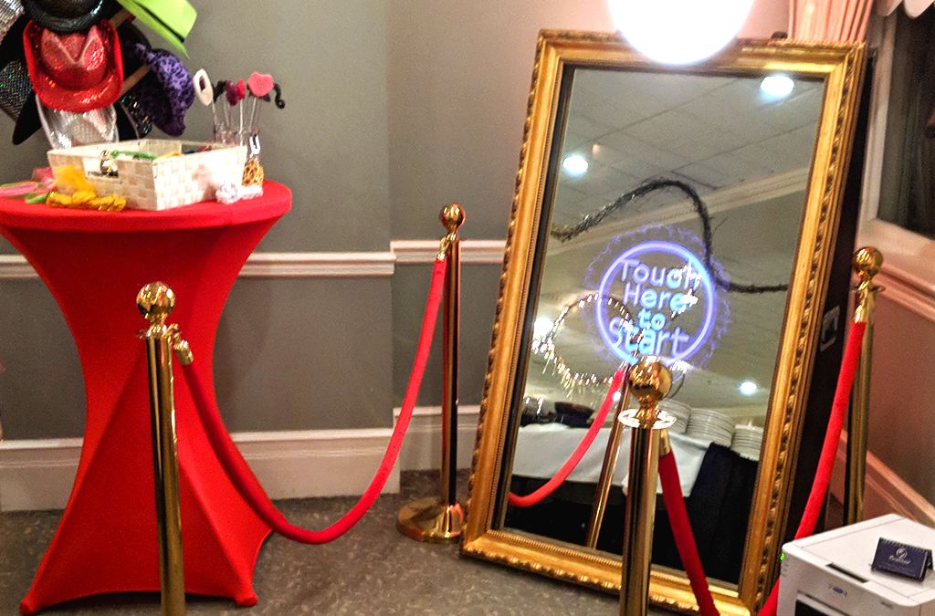 Event setup with a red cocktail table and large gold-framed mirror next to velvet rope stanchions.