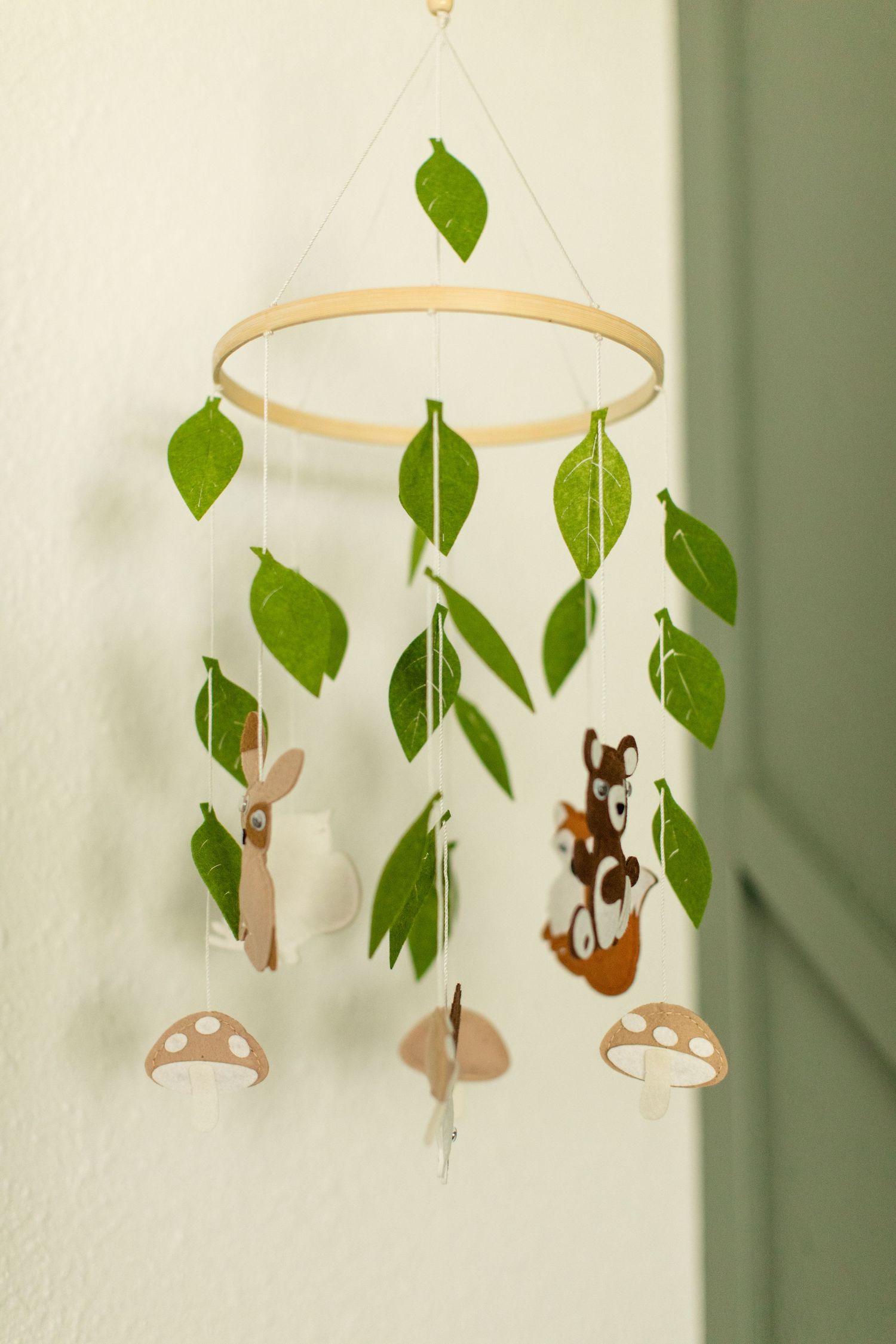 A woodland-themed baby mobile with green leaves and brown mushroom decorations hanging against a wall.