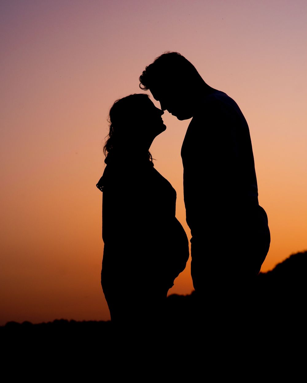 Uniek silhouette bij een prachtige zonsondergang van aanstaande ouders met de zwangere buik