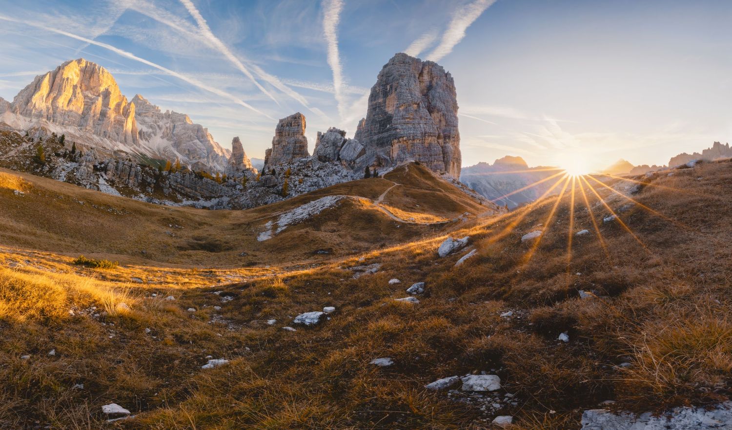 Dramatic sunrise over Dolomites mountains with sun rays bursting through rocky peaks.