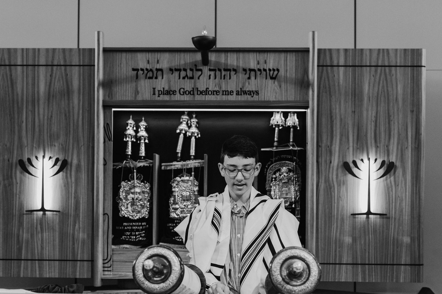 A young boy in a tallit reads from the Torah during his Bar Mitzvah ceremony in synagogue.