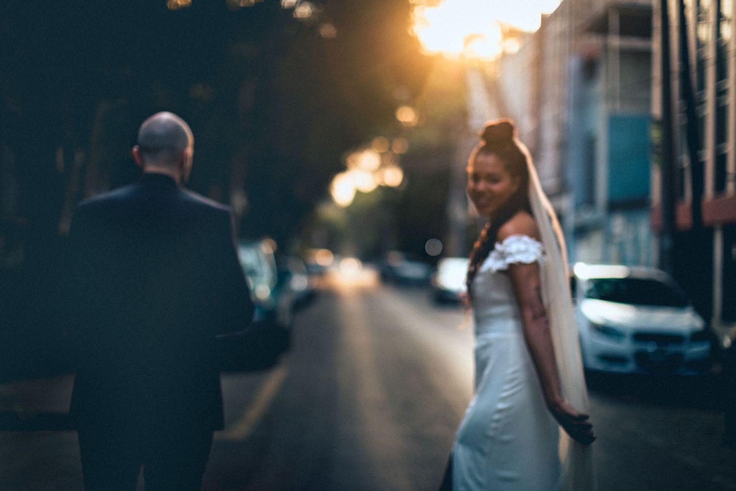 A wedding couple poses on a city street during golden hour with sunlight flare.