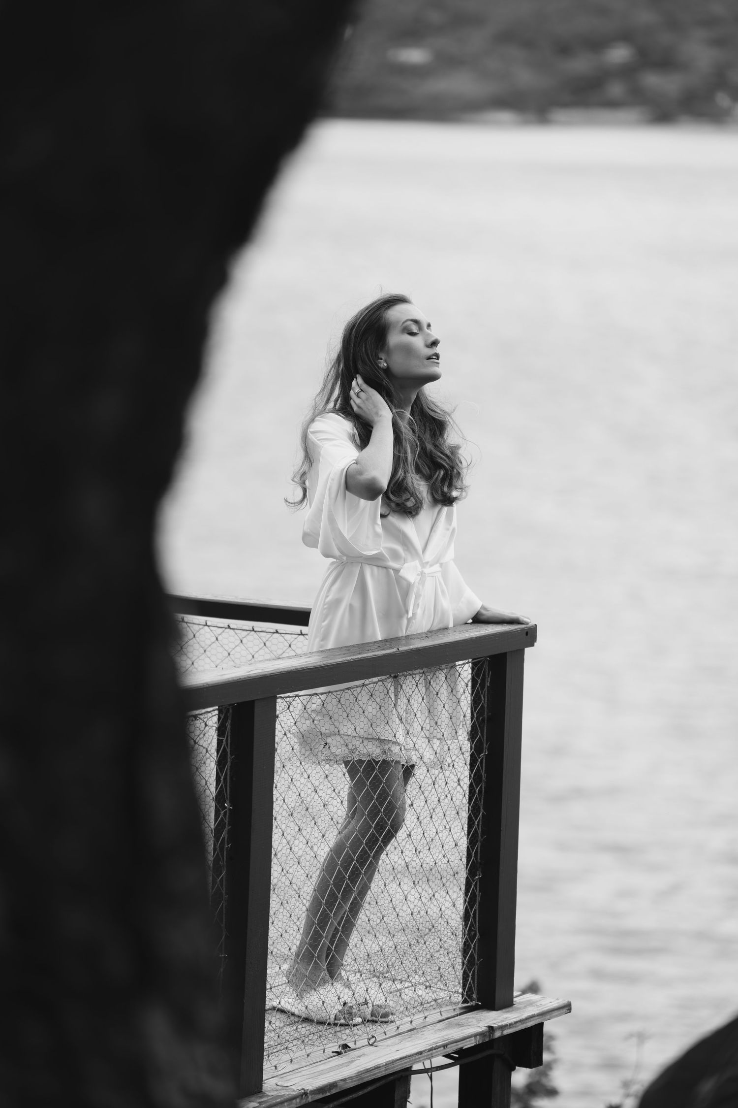 Black and white photo showing silhouette leaning against railing by the water.