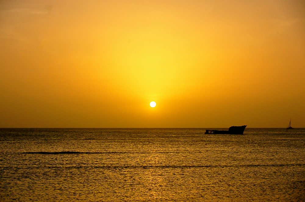 Vibrant orange sunset over ocean waters with boat silhouettes on the horizon.