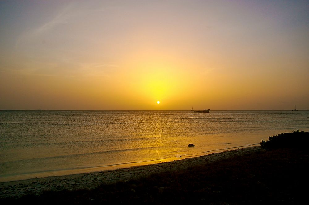 Golden sunset over calm ocean waters with distant boats visible.