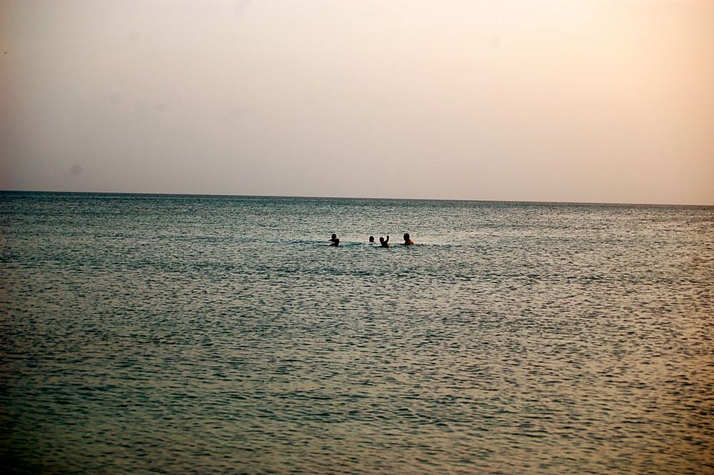 Distant swimmers enjoying calm waters during a peaceful sunset.