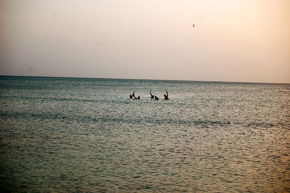 People swimming in tranquil ocean waters during sunset.