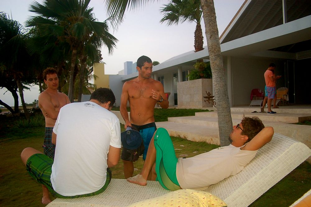People relaxing outdoors on a sunny day near palm trees and modern buildings.