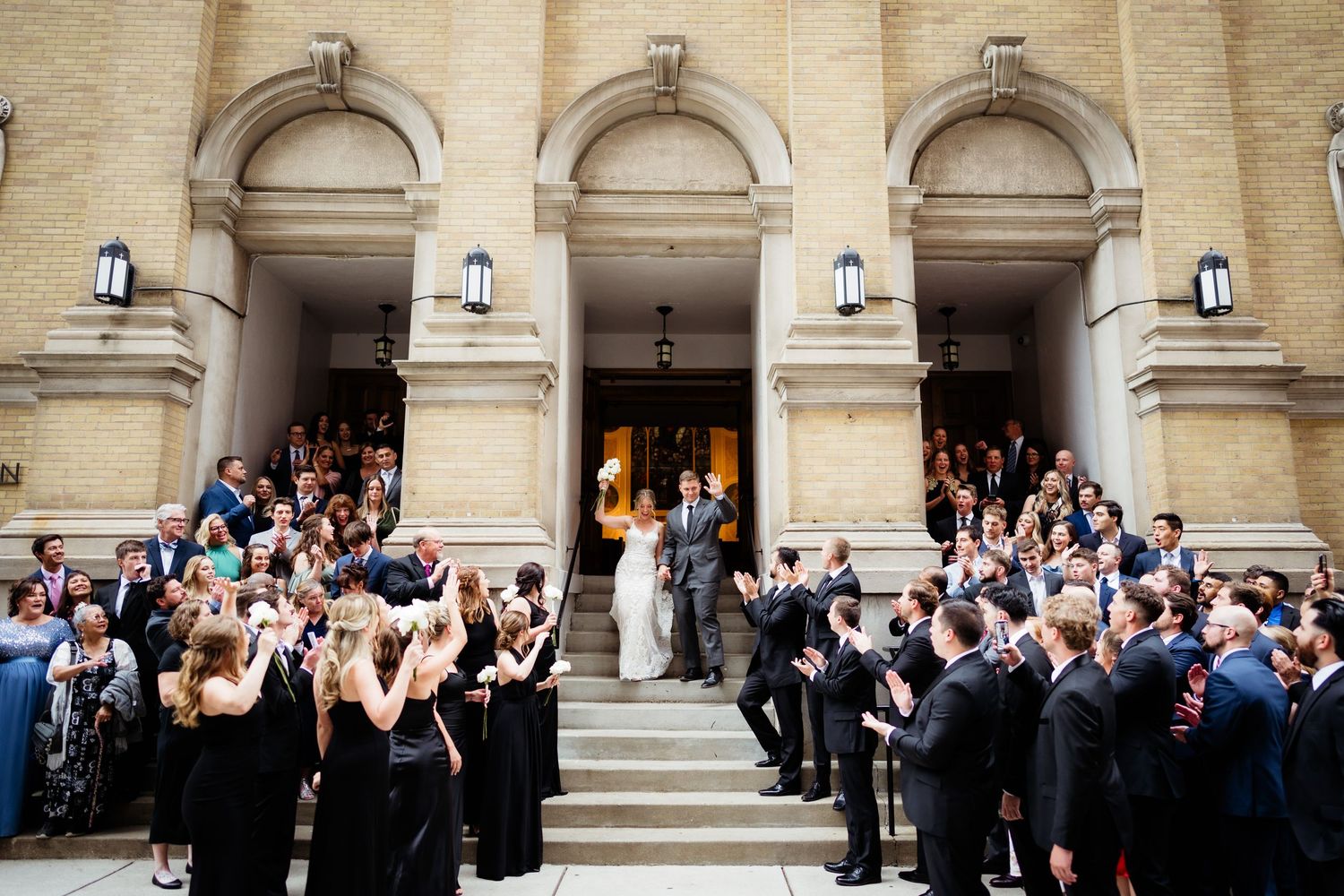 Wedding guests line church steps to celebrate as newlyweds exit the ceremony.
