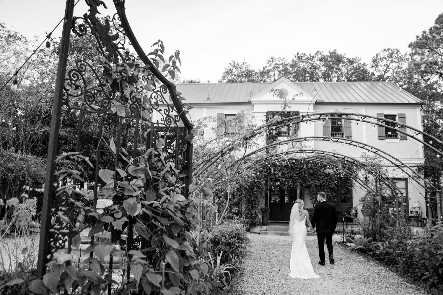A couple walks down a garden path beneath an elegant archway at a romantic black and white wedding venue.