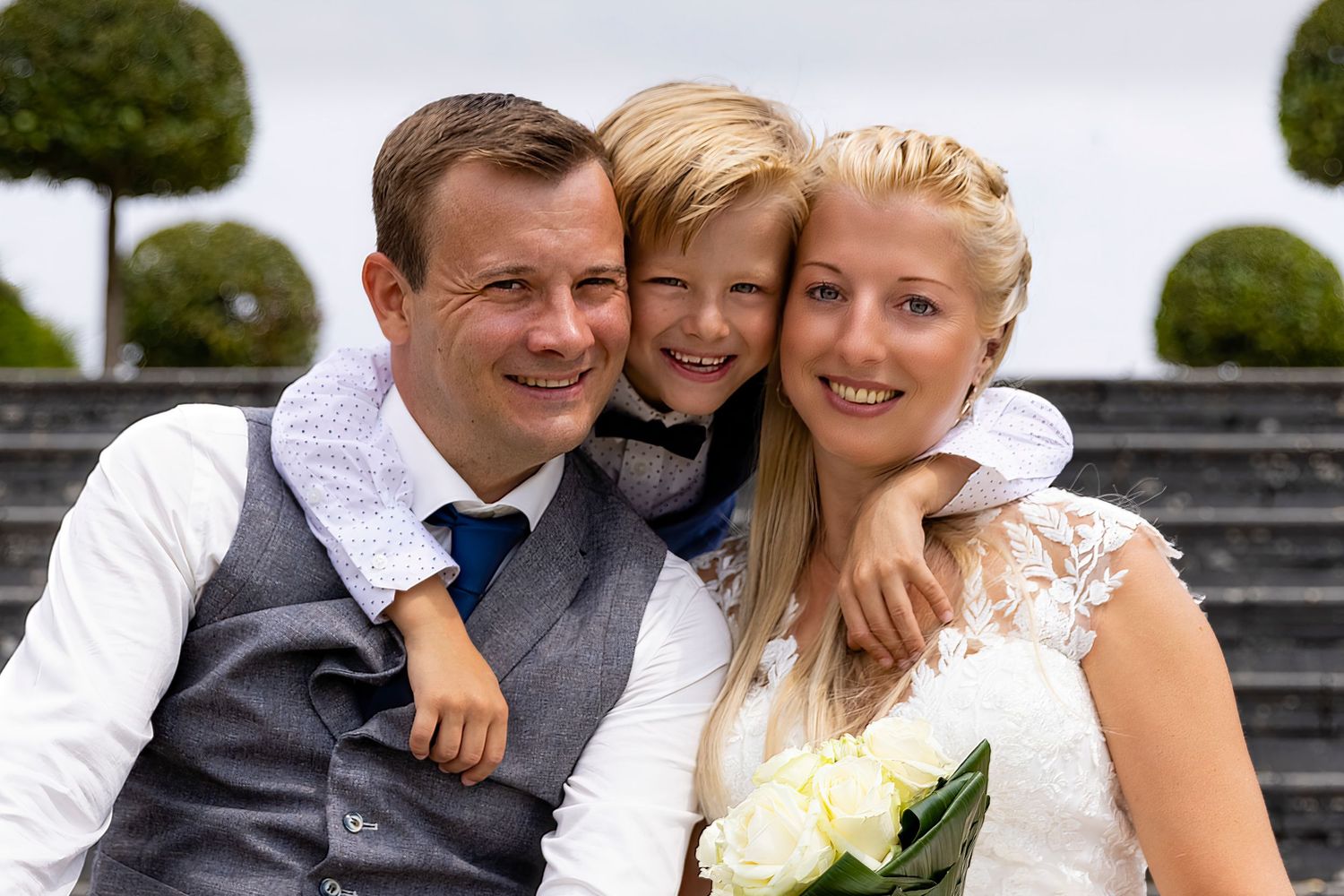 Happy family moment captured outdoors with decorative topiaries in background.