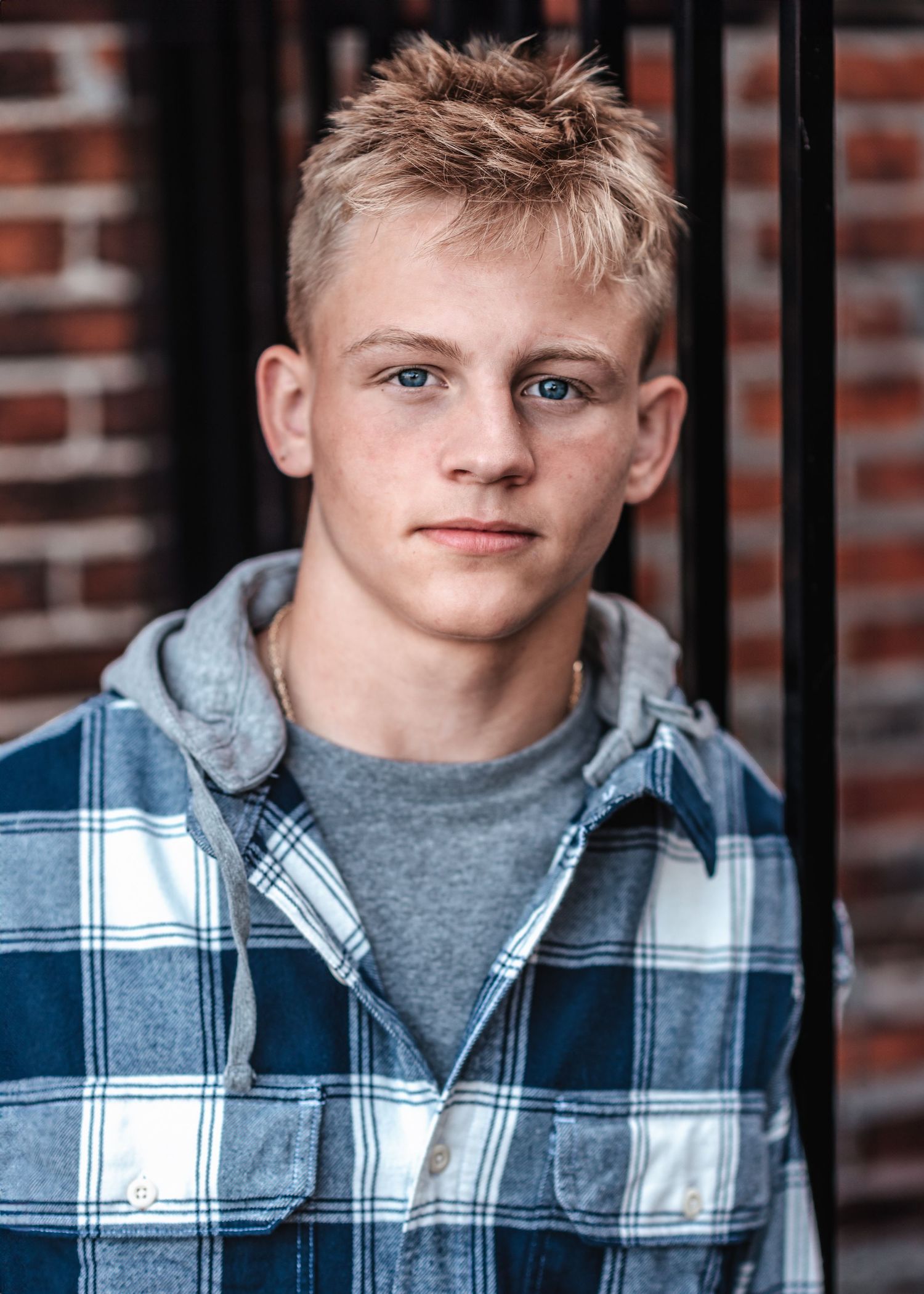 Student wearing plaid flannel and grey shirt poses against brick wall.