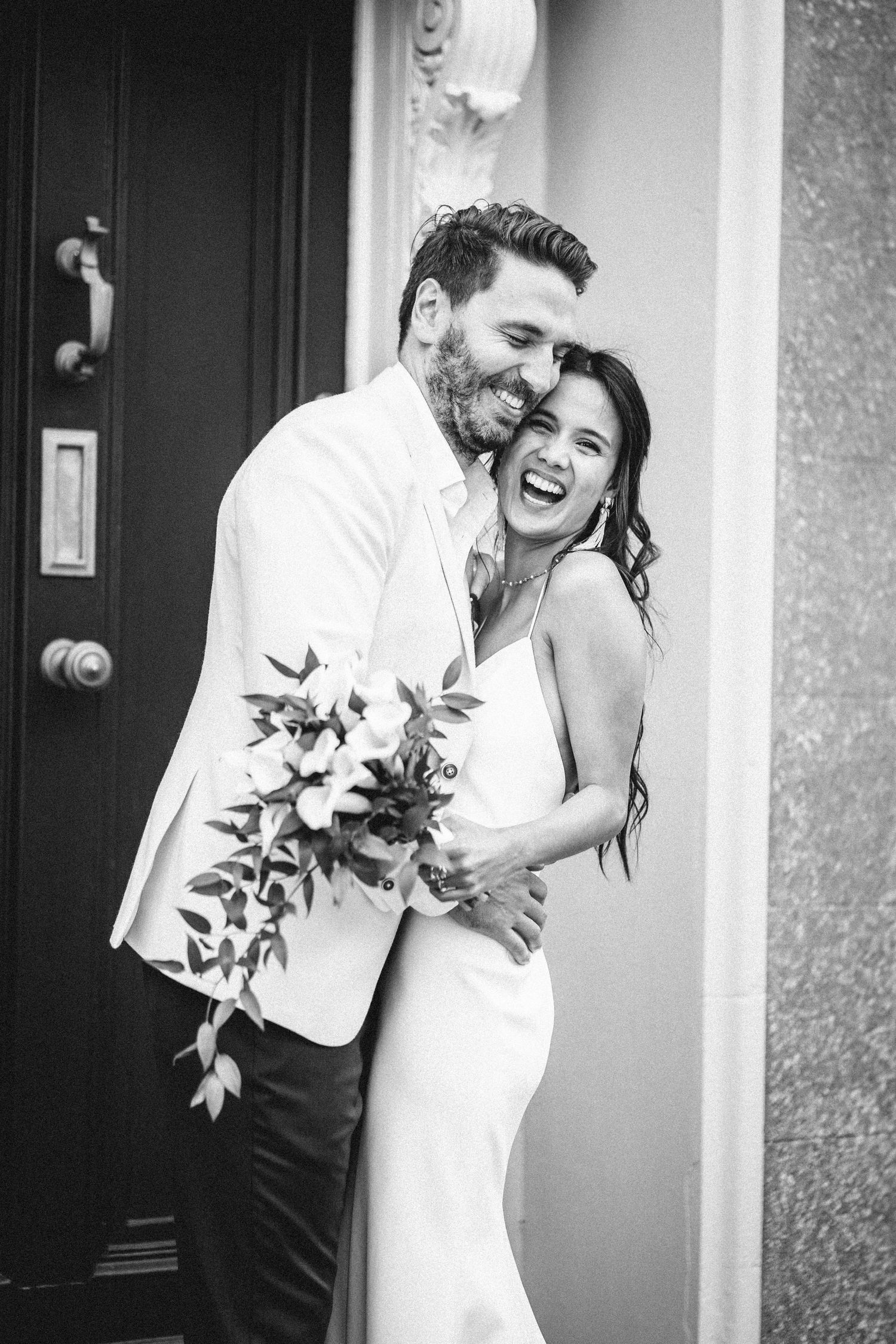 Black and white portrait of joyful couple sharing intimate moment with floral bouquet.