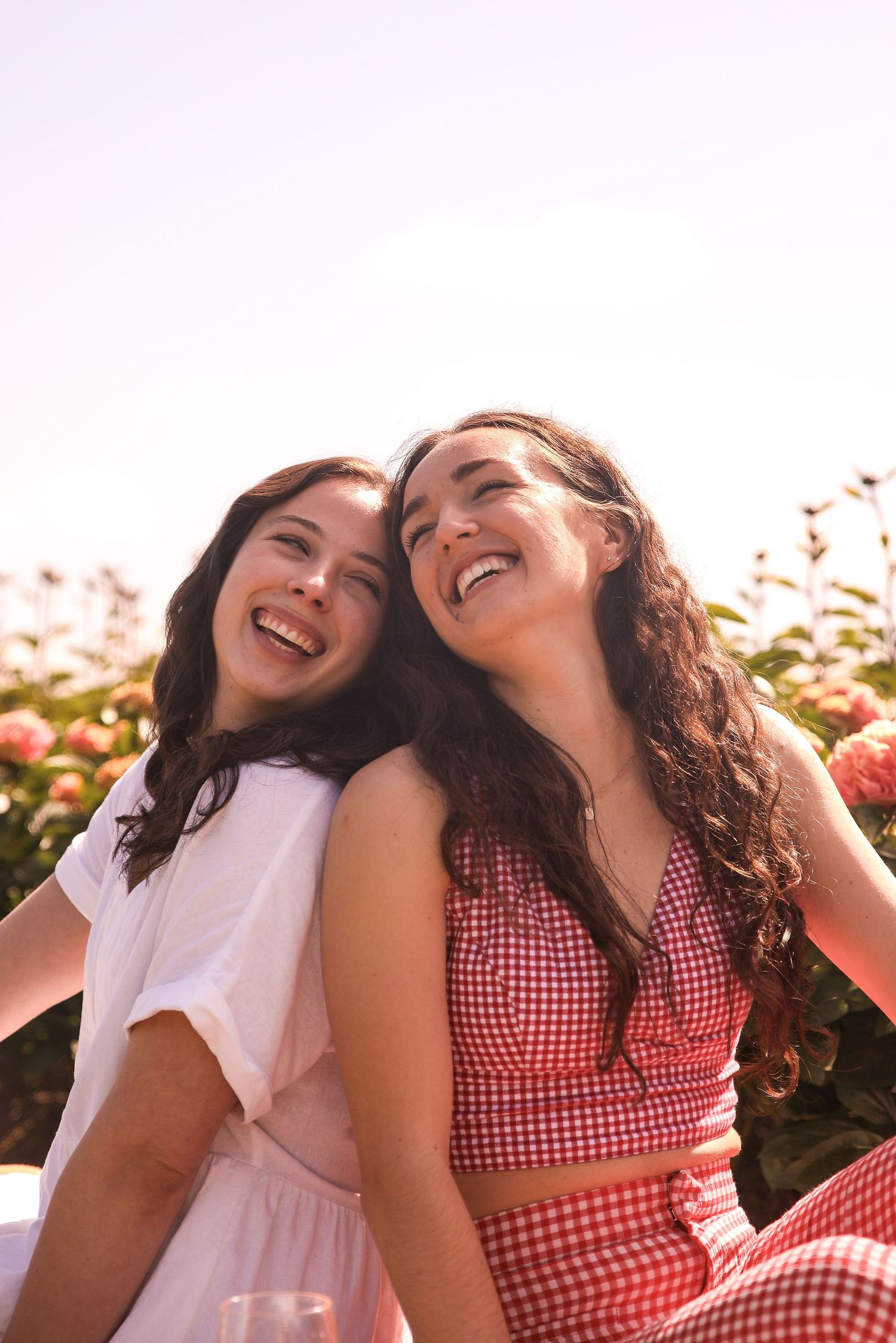 Two friends laughing together during a summer picnic in a rose garden.