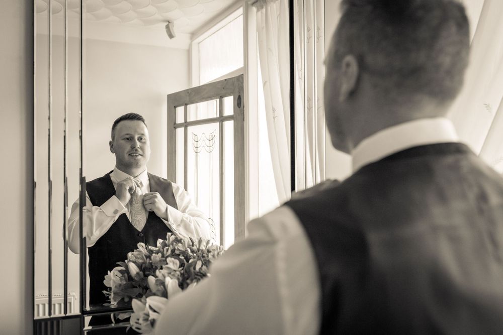 groom straightens his tie reflected in the mirror at home