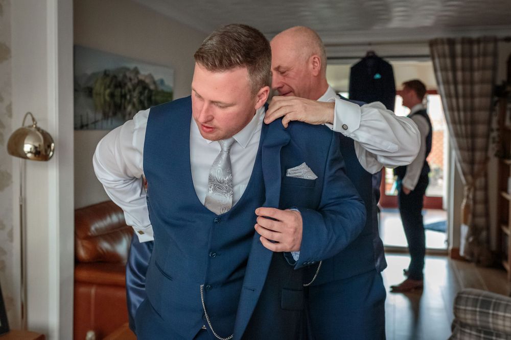 father of the groom helps him put on his jacket
