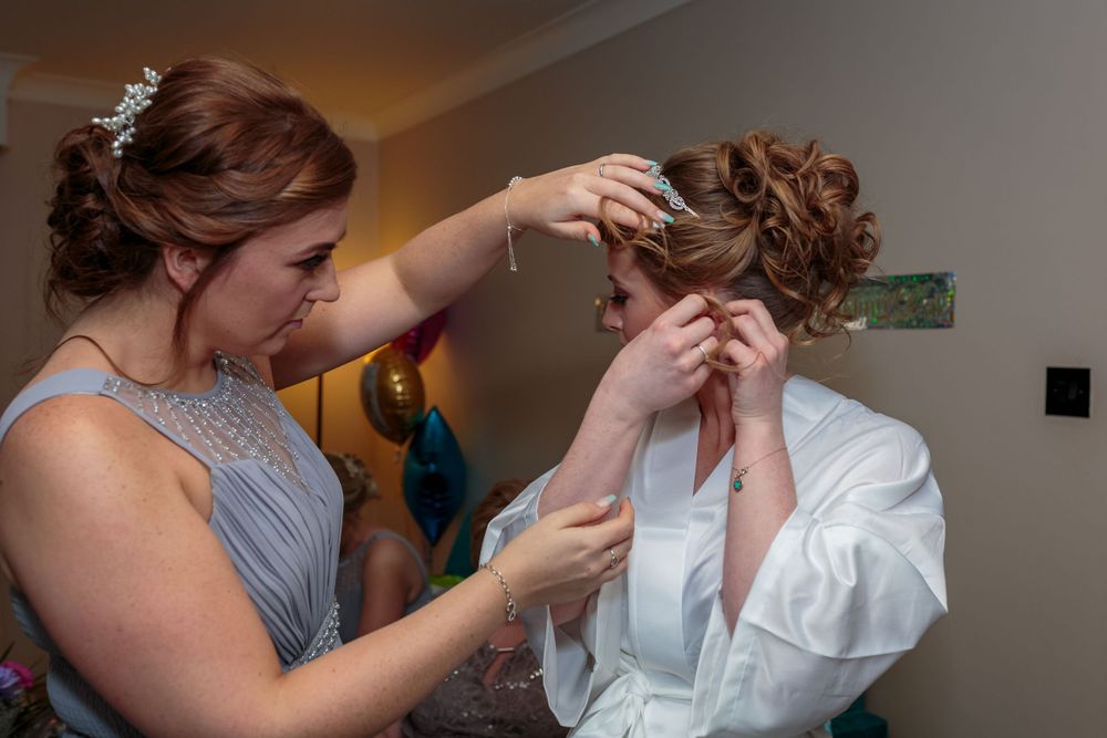 bride puts in her earring helped by her bridesmaid