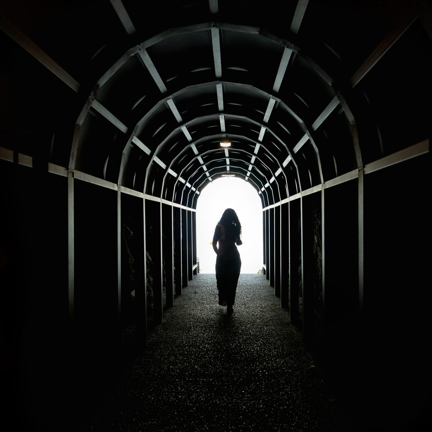 Portrait of a woman in dark wooden tunnel, her black silhouette against bright light, shot by Milwaukee portrait photographer Rachel Dickman