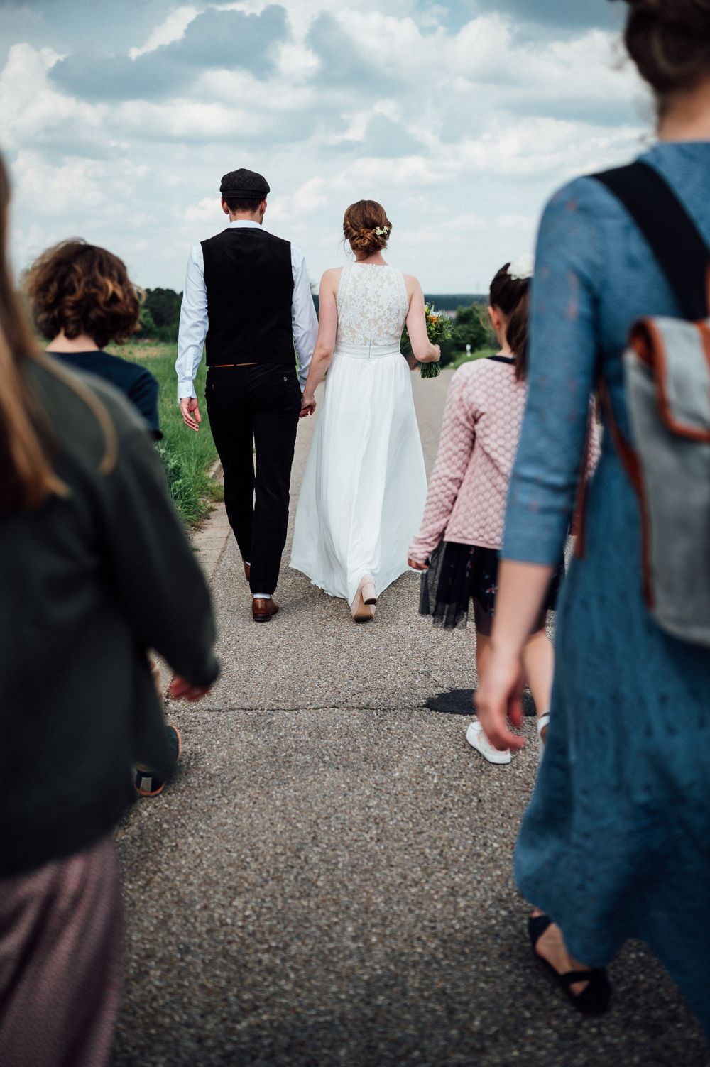A couple in wedding attire walking down a path with guests following behind.