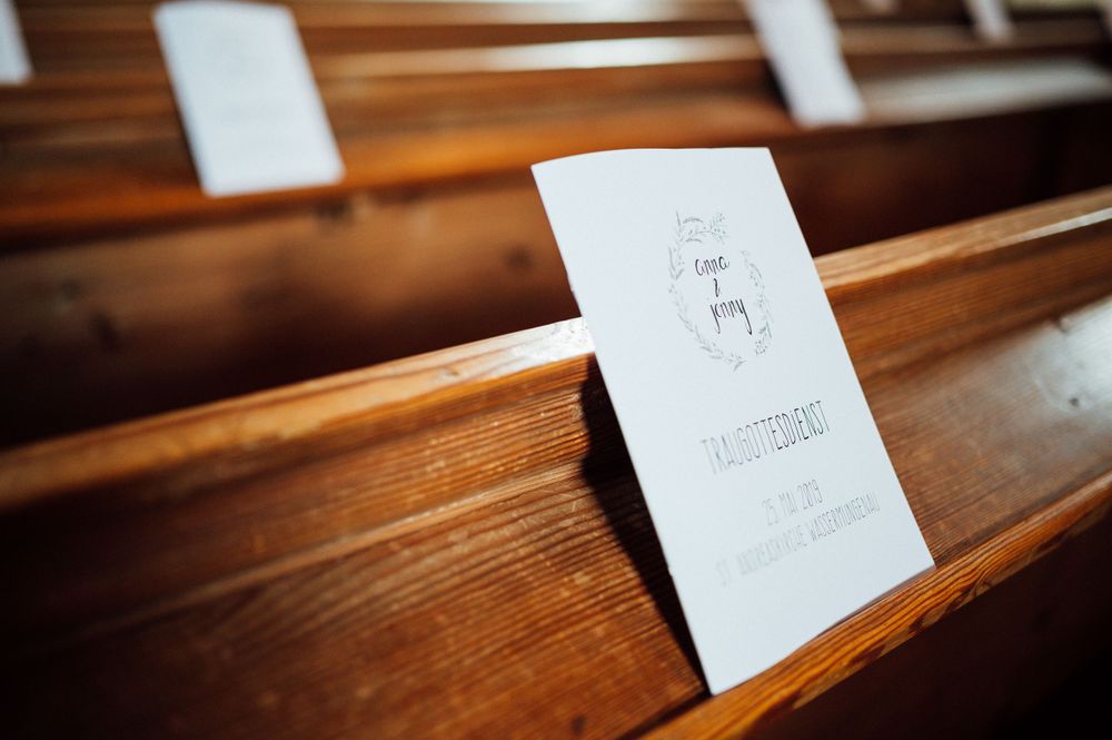 Wedding program booklet resting on wooden church pew.