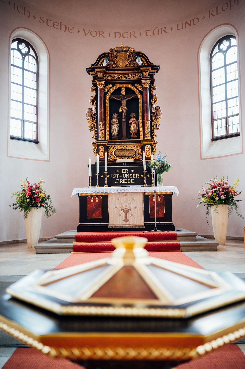 Ornate golden altar with crucifix and floral arrangements in traditional church sanctuary.