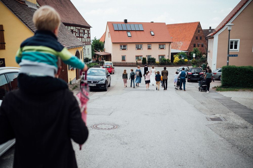 People gathering on a residential street with houses and cars in the background.