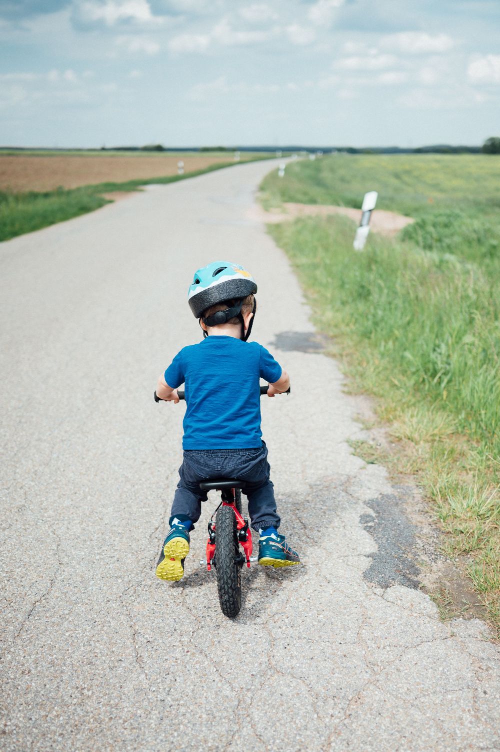 A child riding a bicycle on a country road wearing a blue helmet.