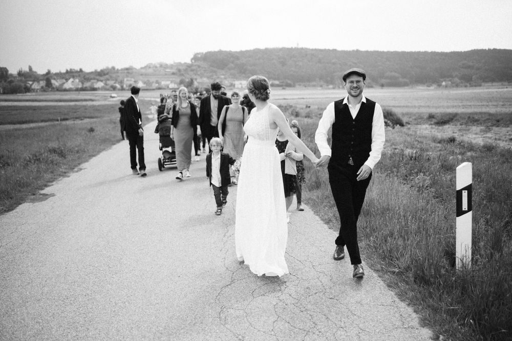 A black and white photo of wedding guests walking along a rural road.