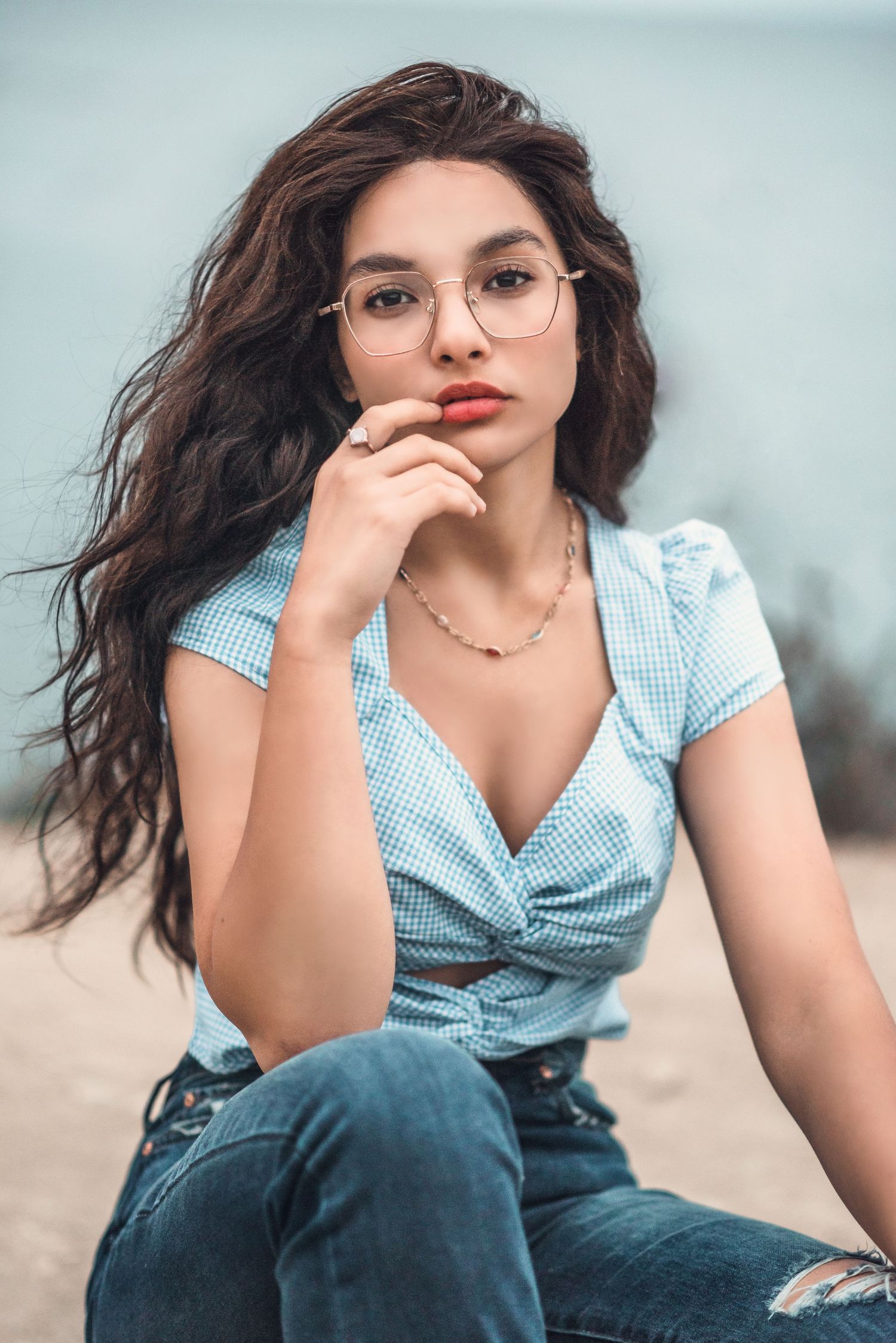 Fashion portrait of woman in blue wrap dress and round glasses with long dark hair.
