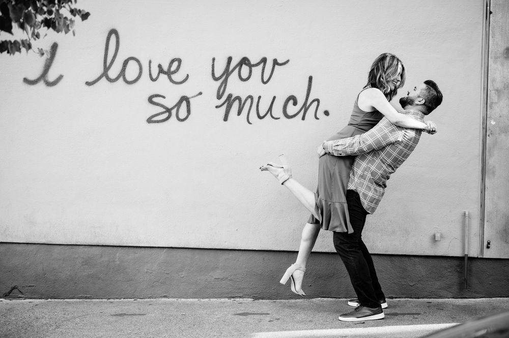 A romantic black and white photo against a wall with 'I love you so much' written on it.Congress Avenue Engagement session Austin