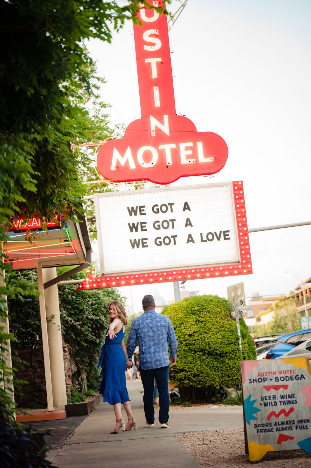 Couple walks beneath vintage Austin Motel sign with romantic message board.Congress Avenue Engagement session Austin