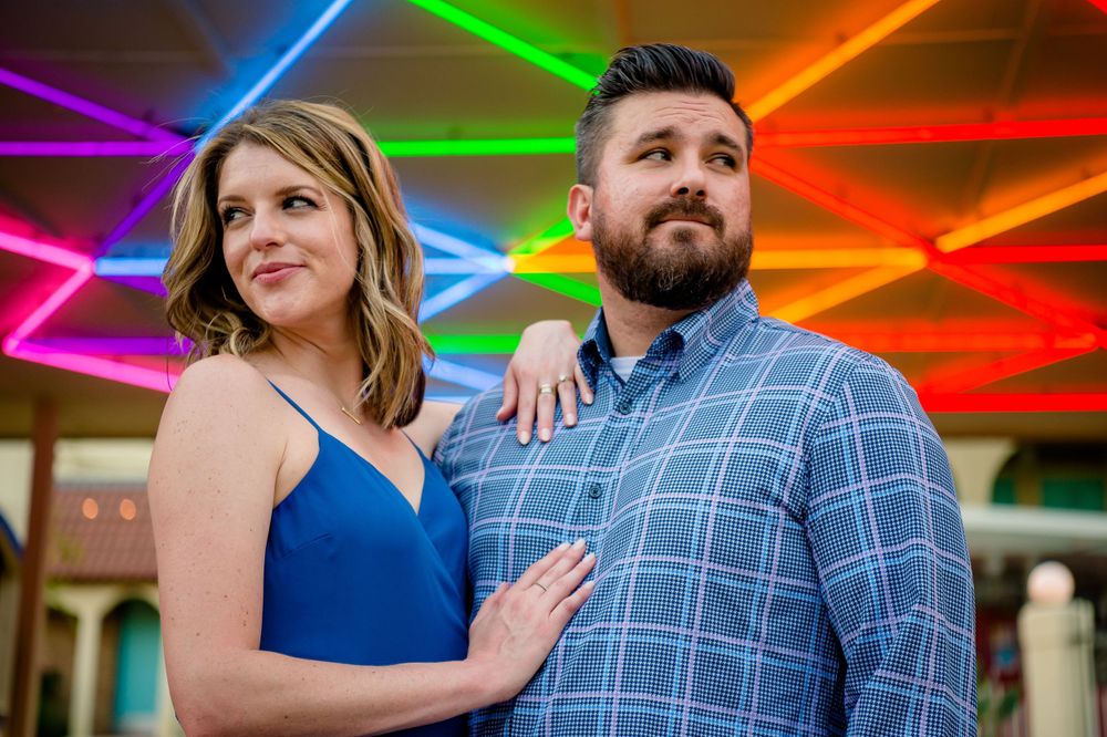 Couple poses against vibrant neon lighting display creating a colorful geometric pattern.Congress Avenue Engagement session Austin