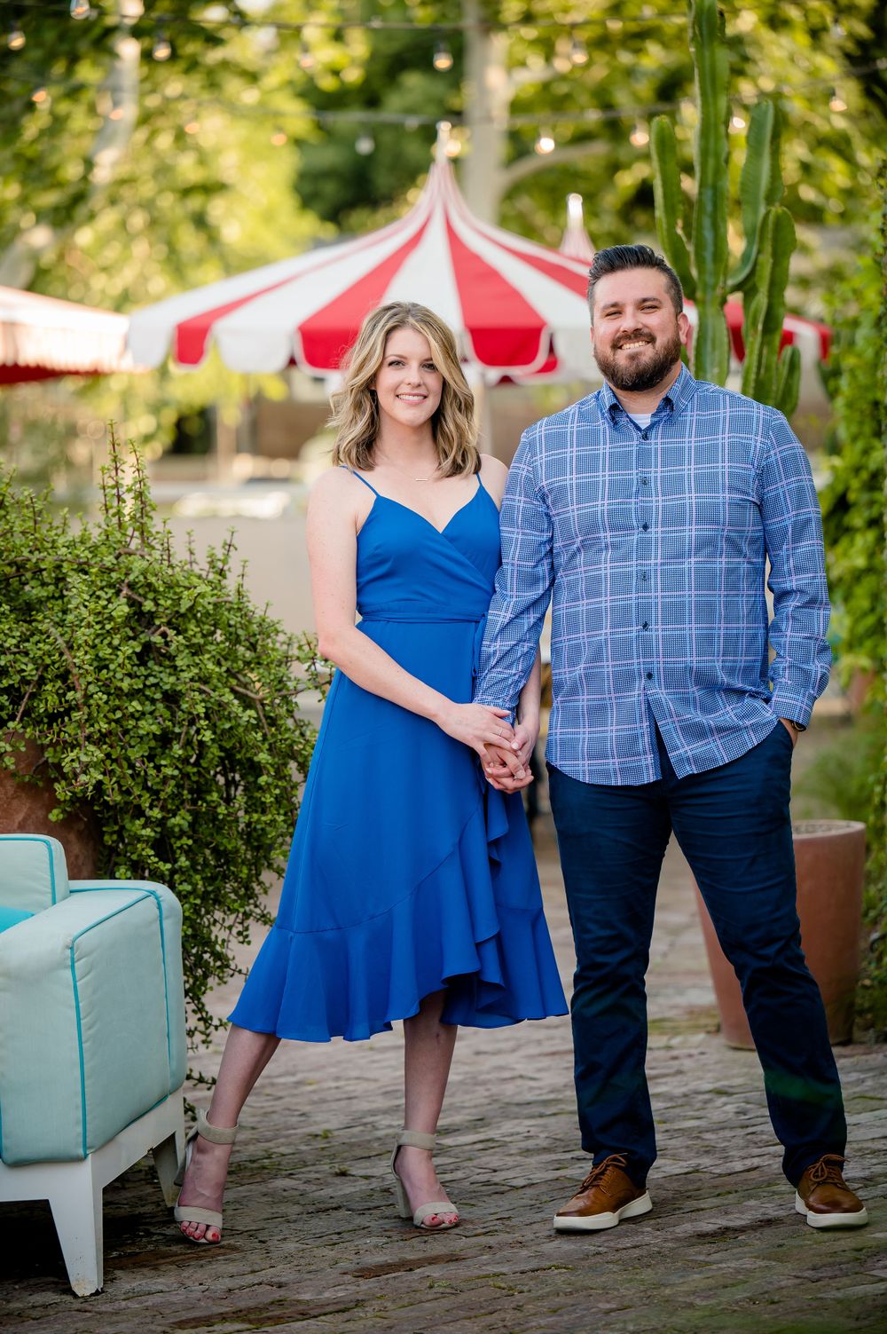 A couple poses together outdoors, with a red and white striped tent and greenery in the background.Congress Avenue Engagement session Austin