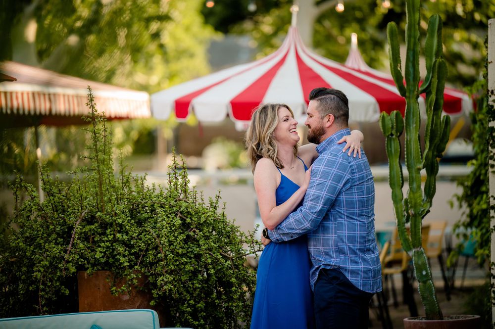 A romantic couple embraces beneath a red and white striped tent in a lush garden setting.Congress Avenue Engagement session Austin