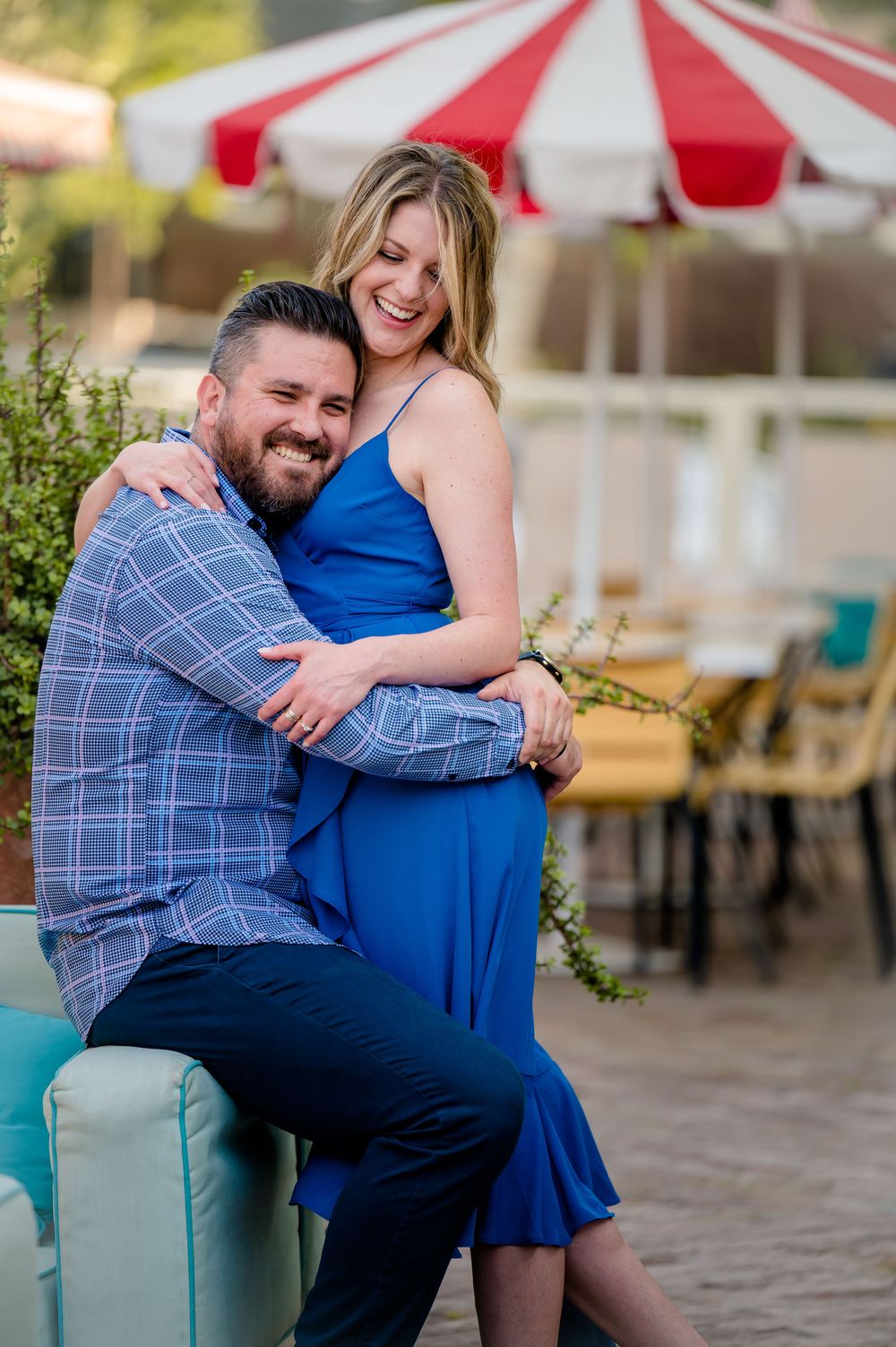 Couple laughing together on patio with striped umbrella in background.Congress Avenue Engagement session Austin