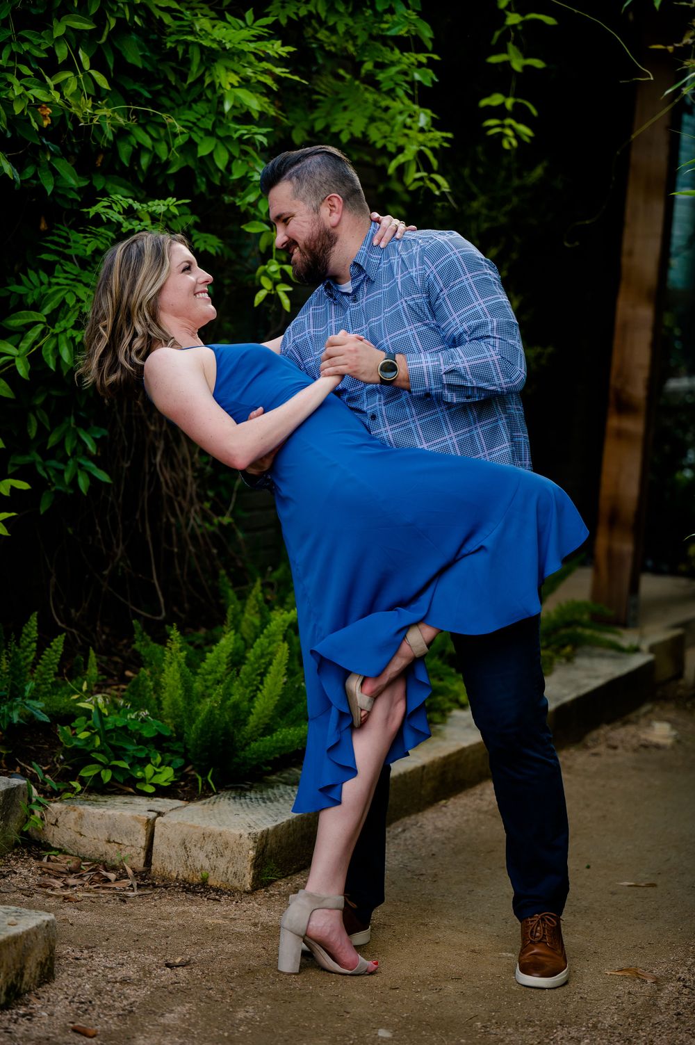 Dancing couple in blue dress and plaid shirt sharing playful moment outdoors.Congress Avenue Engagement session Austin