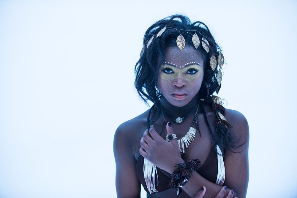 A mystical portrait with decorative face paint and tribal-inspired accessories against a white background.