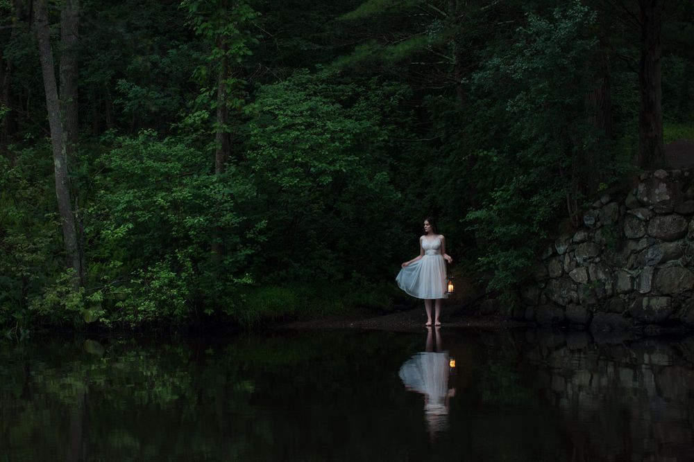 A dreamy scene of a figure in a white dress standing on water in a dark forest.