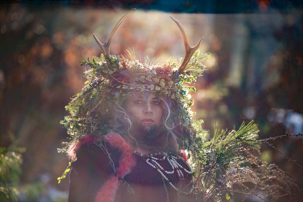 A mystical portrait with antlers and foliage crown illuminated in golden light.