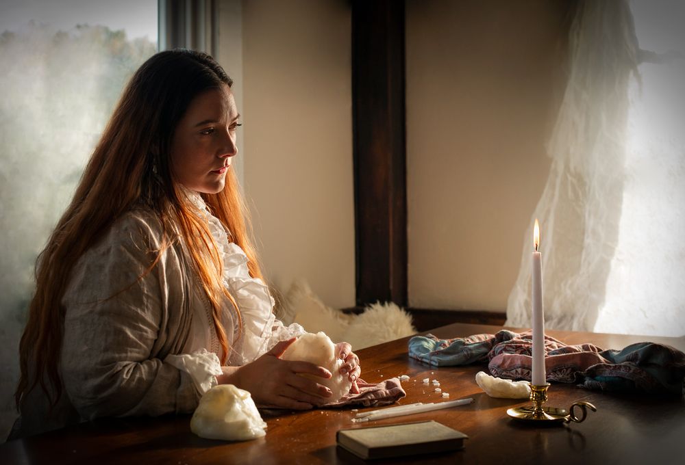 A candlelit scene showing someone writing at a desk in vintage attire.