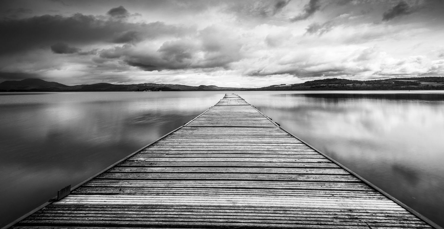Black and white photo of a wooden pier extending into a calm reflective lake.