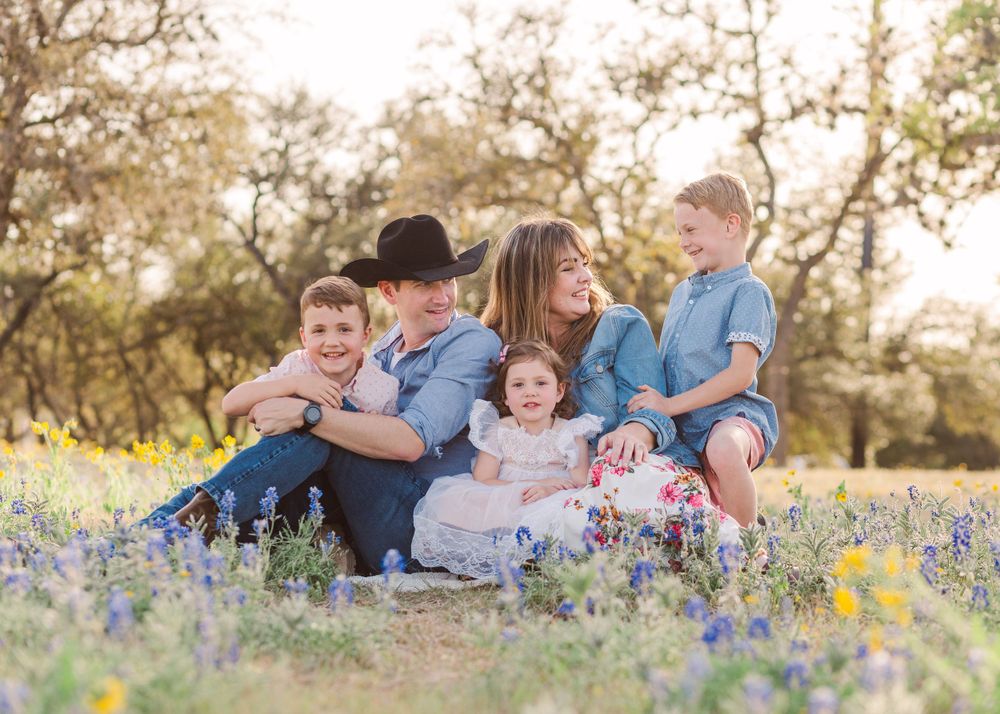 Family relaxes together in blooming wildflower field during sunset photo session.