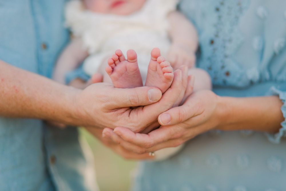Close-up of hands gently holding baby's feet against blue fabric background.