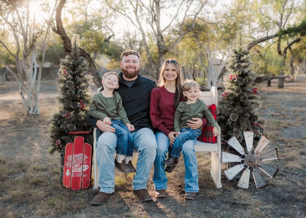 Family of four posed together on rustic bench with holiday decorations.