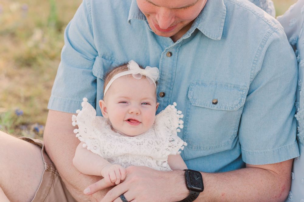 Close-up portrait of parent and baby in light blue clothing outdoors.