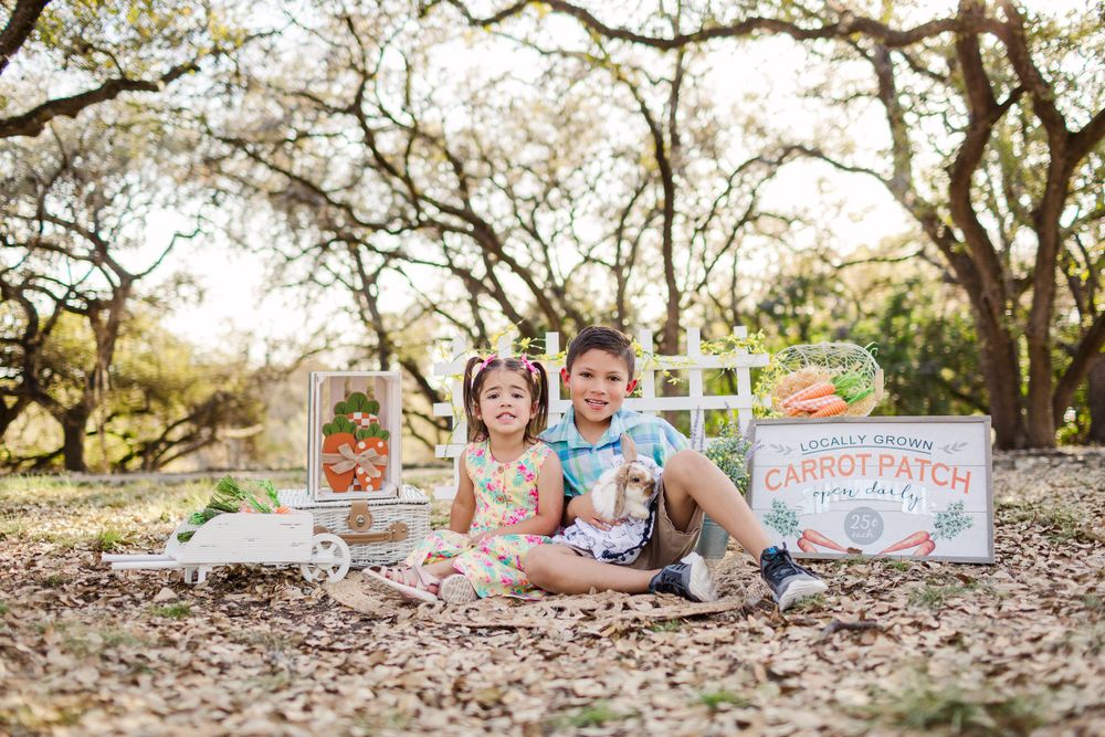 Children sitting on blanket with fall props and pumpkins during outdoor photo session.