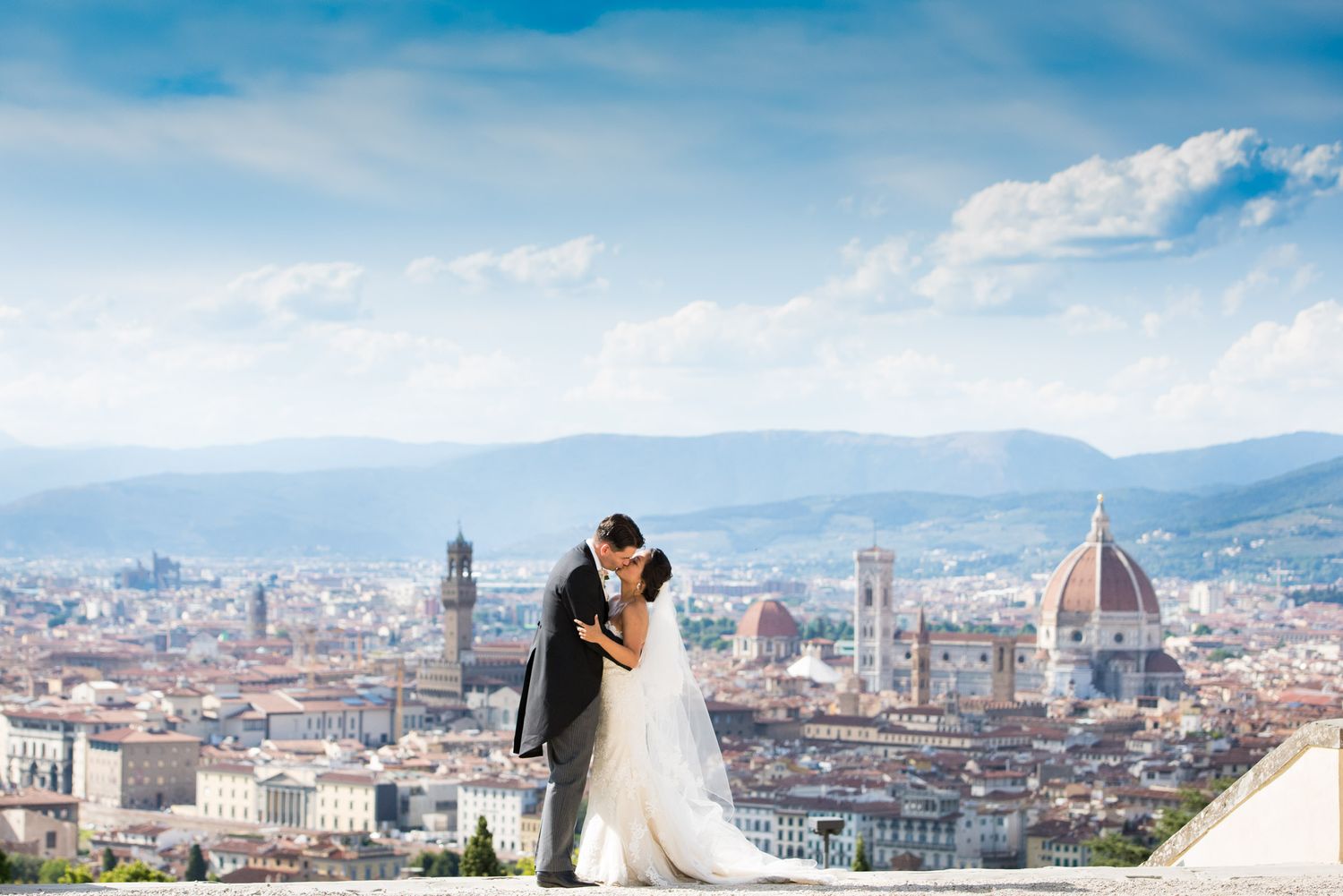 A scenic view of Florence, Italy with the iconic Duomo cathedral dome and city skyline against mountains and blue sky.