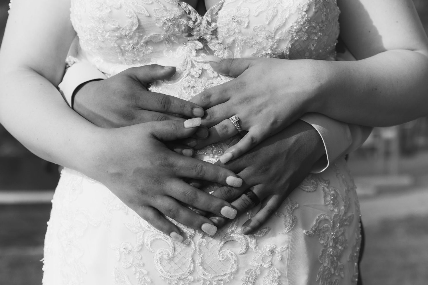 Detail shot of hands with wedding rings against white lace dress.