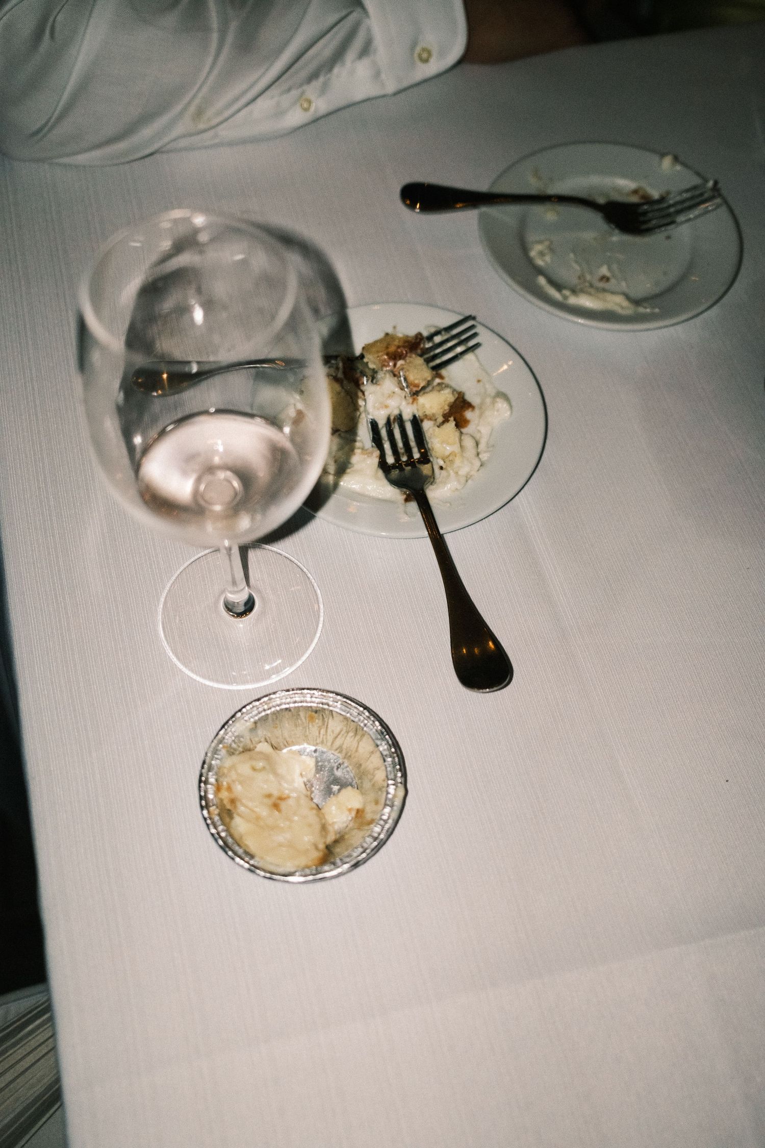 Partially eaten food and wine glasses on a white tablecloth at a formal dining setting.